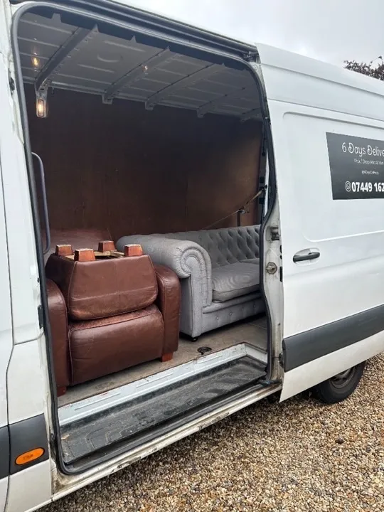 Furniture collection — sofa and armchair delivery Brown leather armchair and grey tufted sofa loaded through the side door of a furniture collection van