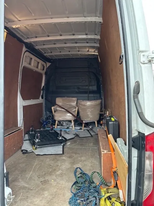 Furniture collection — wrapped armchairs Two upholstered armchairs wrapped in protective plastic inside a furniture collection van with dollies and straps