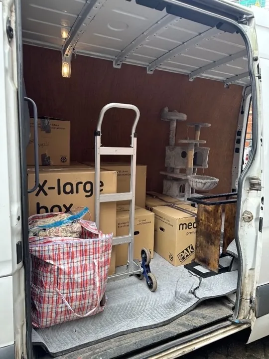 House removals — packed van with stair climber House removals van interior with labelled moving boxes, a cat tree, and a stair-climbing hand truck on protective moving blankets