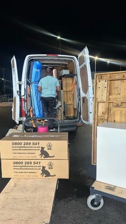 Long-distance moves — night van loading Crew loading a removals van at night with furniture wrapped in protective plastic and secured with ratchet straps for a long-distance UK move
