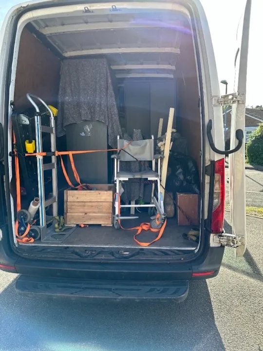 Furniture collection van — strapped load Professional furniture collection van loaded with wardrobe, shower chair, and household items secured with ratchet straps